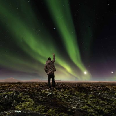 Man in a Lava Field in Iceland Raising His Arm to the Sky With Dancing Northern Lights