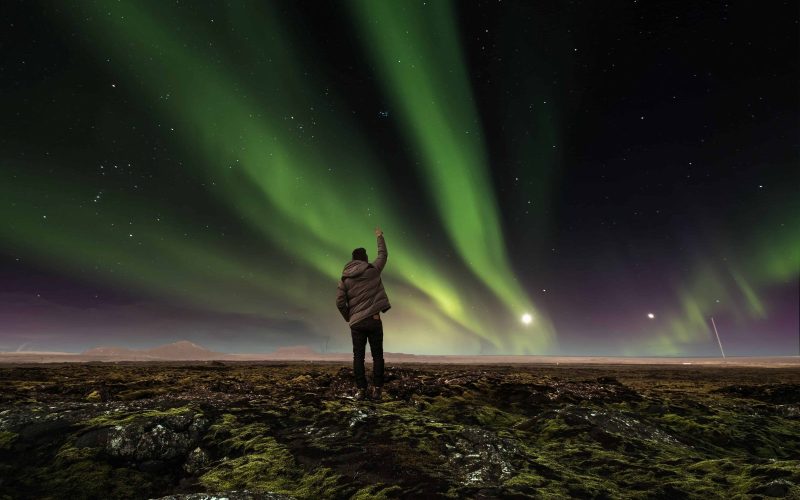 Man in a Lava Field in Iceland Raising His Arm to the Sky With Dancing Northern Lights