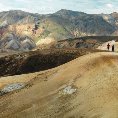 Couple Walking Towards Colorful Mountains In Landmannalaugar In The Icelandic Highlands