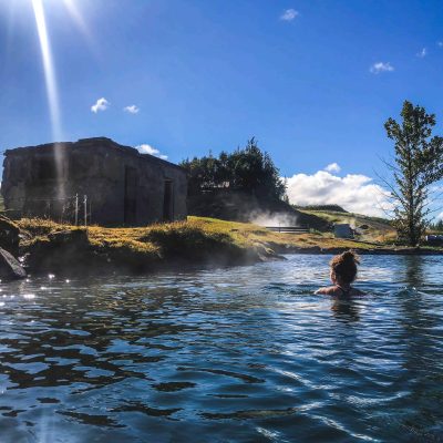 Woman Bathing In The Hot Waters Of The Secret Lagoon, A Natural Hot Pool On The Golden Circle In Iceland On A Sunny Day